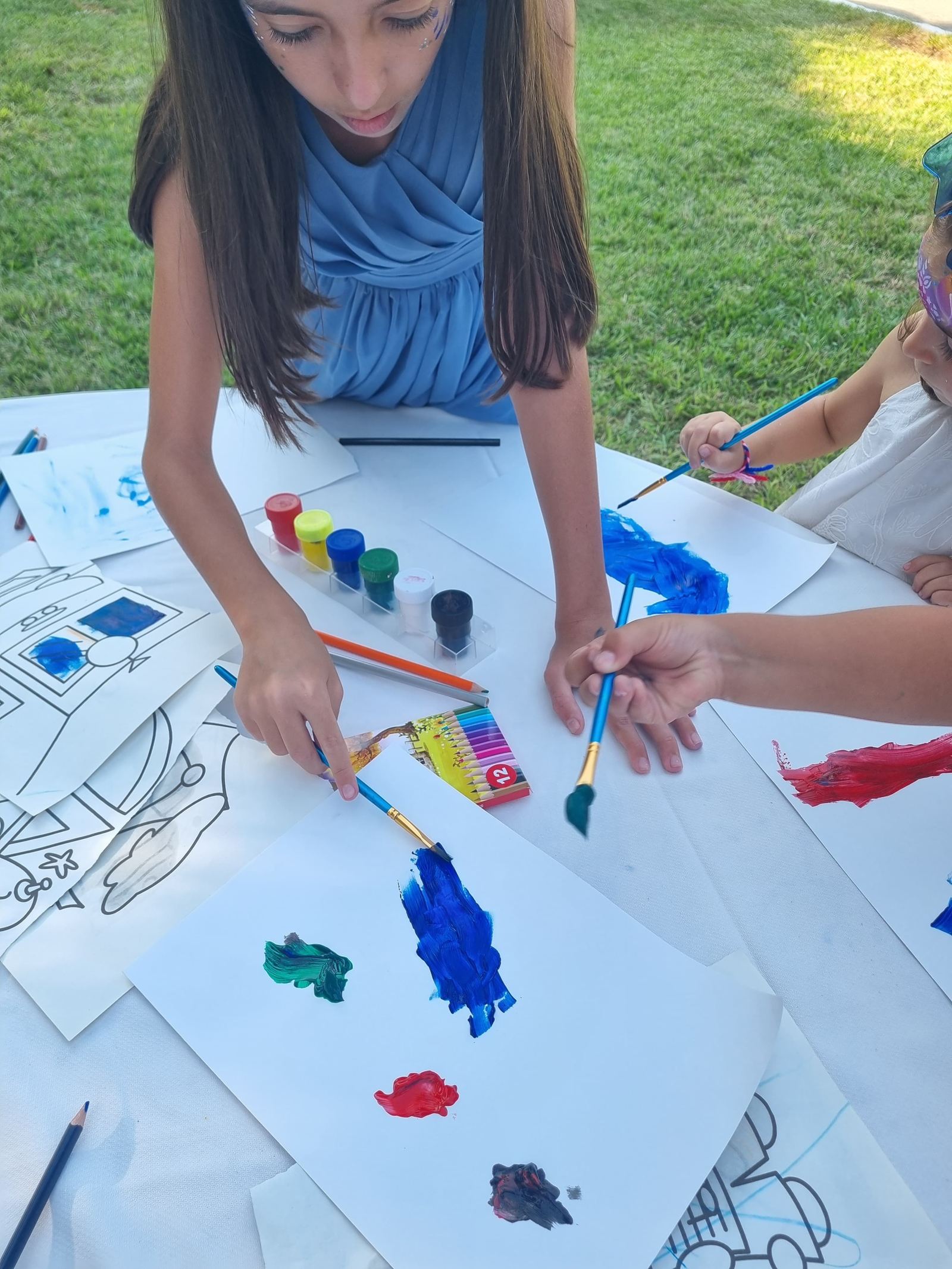 Crianças a pintar com pincéis e tintas numa mesa de ateliê